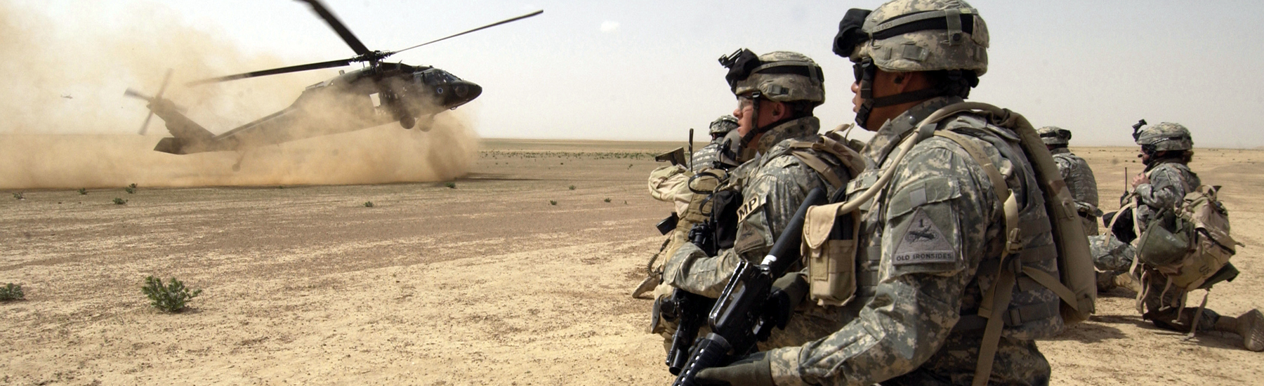 A military helicopter lands in the desert.